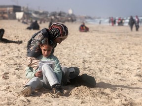 A Palestinian woman and a girl sit along a beach adjoining a makeshift camp for displaced people in Rafah in the southern Gaza Strip on Saturday, March 30, 2024, amid the continuinmg conflict between Israel and the militant group Hamas.