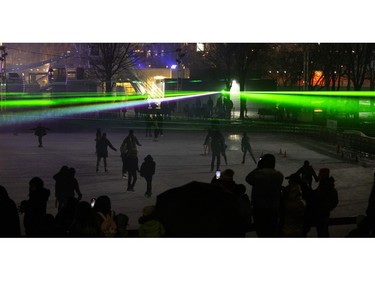 People watch as others skate under a laser show that is meant to replicate the Northern Lights during a nuit blanche in the Old Port in Montreal on Saturday, March 2, 2024.