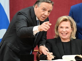 Coalition Avenir Quebec MNA Martine Biron smiles as Quebec Premier Francois Legault grabs her hand and points toward photographers so she can pose for an official picture, Tuesday, October 18, 2022 during a ceremony at the legislature in Quebec City. National Assembly secretary general Siegfried Peters, right, looks on. THE CANADIAN PRESS/Jacques Boissinot