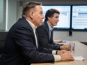 Quebec Premier François Legault and Prime Minister Justin Trudeau are seen in profile leaning on a table in front of two screens displaying Hydro-Québec statistics.