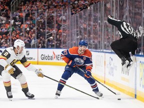 Golden Knights' Zach Whitecloud, left, and Oilers' Connor McDavid battle for the puck near the blue line as a linesman jumps out of the way during a game last year.