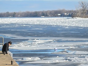 A man sits on a dock next to an icy canal on a sunny day