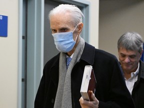 Jacques Delisle wears a medical mask and holds a book as he walks down a corridor