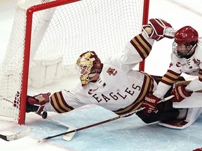 A goalie in an Eagles jersey reaches back toward the corner of the net to stop a puck