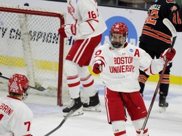 Boston University defenceman Lane Hutson smiles and points to a teammate beside the goal