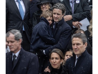 Nicolas Mulroney, son of Brian Mulroney, holds a child as the casket of Canada's 18th prime minister, Brian Mulroney, is taken away at Notre-Dame Basilica on Saturday, March 23, 2024. On the bottom right is Mark Mulroney.