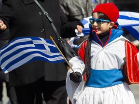 A child wearing Greek colours walks in a parade.