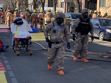 People in hazmat suits on a closed street. There is a stretcher behind them.