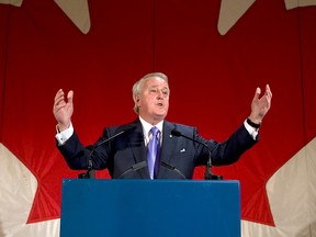 Brian Mulroney speaks at a lectern in front of a giant Canadian flag