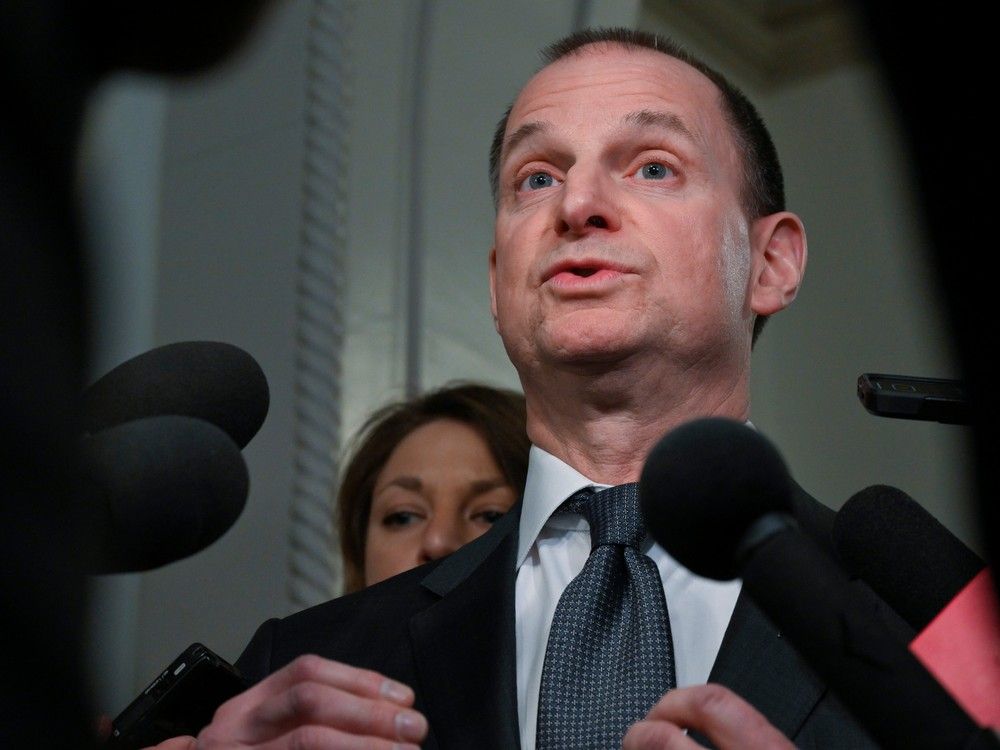 a while man is standing in front of microphones and his mouth is open as if speaking.