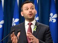 Paul St-Pierre Plamondon gestures at a podium in front of a backdrop of Quebec flags.