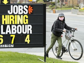 A cyclist moves past a jobs advertisement sign in Toronto on Wednesday, April 29, 2020.
