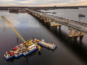 A bridge is visible to the right of the photo and to the left, there is a platform in the water with a crane and other construction materials on it.