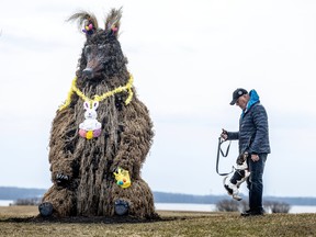 A small dog jumps on its human. they are standing next to a sculpture of a bear with an Easter bunny around its neck.