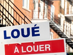 A for rent sign on a residential property in Montreal is seen in the bottom left of the photo with a bricked building in the background with staircases going down.