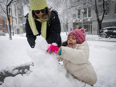 A young girl builds a snowman as a woman helps on a snowy day