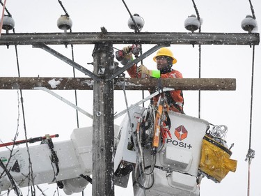 A worker is seen working on power lines in the snow