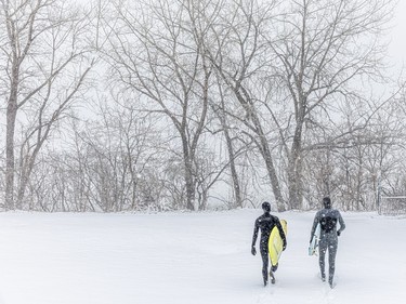 Two people with surfboards head to the water during a snowstorm