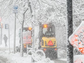 Snow removal vehicles make their way down the street as snow continues to fall.