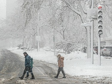 People cross a street in the snow.