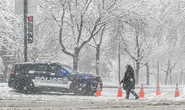 A police car and orange cones block a snow-covered street.
