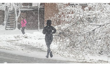 A person jogs on a snowy street, past a fallen tree.