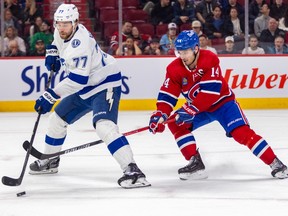 Canadiens' Nick Suzuki, wearing the Habs' red home jersey, has his stick between the legs of Lightning defenceman Victor Hedman, as the defenceman is seen handling the puck.