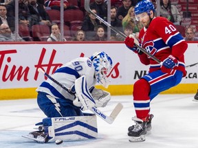 Canadiens' Joel Armia, wearing the Habs' home red jersey, is seen with his stick in the air, lurking in front of crouching Lightning goalie Matt Tomkins. He is clearly looking for a rebound, with the puck seen off to the right of the goalie's pad.