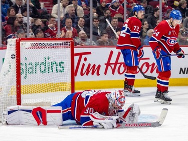 Montreal Canadiens' Cayden Primeau lays on the ice while two Canadiens players skate away dejected