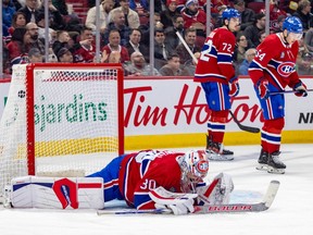 Montreal Canadiens' Cayden Primeau lays on the ice while two Canadiens players skate away dejected