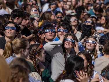 A crowd of people wear eclipse glasses.