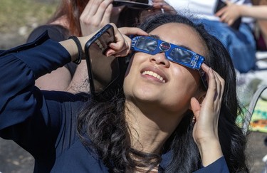A woman wearing eclipse glasses stares up.
