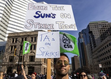 A man holds signs reading Even the Sun's on Strike Today and TAs on strike.