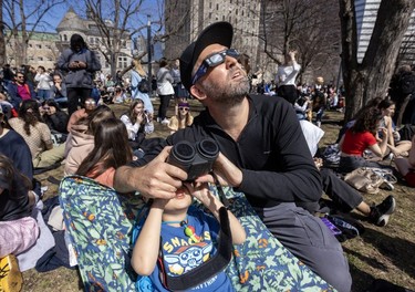 Michael Smith, from Los Angeles, helps his son Nolan watch the eclipse on the campus of McGill University in Montreal Monday April 8, 2024.