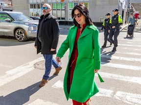 Valérie Plante, wearing a green coat and sunglasses, crosses a street on a sidewalk with police officers behind her.