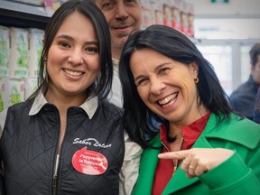 Montreal Mayor Valerie Plante smiles and points to a sticker on a store employee's uniform indicating the employee is taking French lessons.