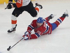 Tanner Pearson extends his stick toward the puck while lying on the ice as a Flyers player skates next to him