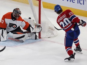 Canadiens' Juraj Slafkovsky, wearing the Habs' red home jersey, is seen with his stick in the follow-through position to the left of Flyers' goalie Samuel Ersson with the puck seen behind Ersson in the mesh of the net.