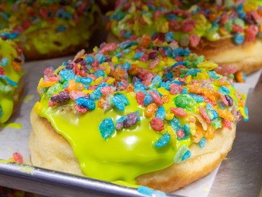 Colourful sprinkles cover donuts with a yellow-green glaze on a tray