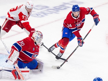 Canadiens' Logan Mailloux skates with the puck in front of Canadiens goalie Cayden Primeau while a Red Wings player tries to get his stick in the play