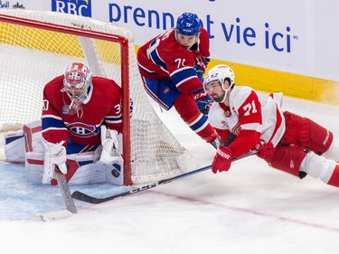 Detroit Red Wings' Dylan Larkin falls to the ice beside the net while the puck is on the pad of a Canadiens goalie and Canadiens' Jake Evans chases from behind the net