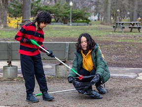 A child uses a picker-upper to put garbage into a bag held by a woman in a park.