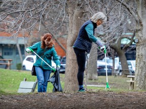 Two women collect litter with long tongs in a park, under a flowering tree.