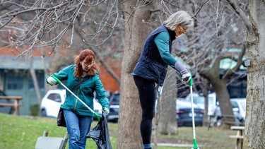 Two women collect litter with long tongs in a park, under a flowering tree.