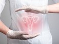 A person in white, with white gloves holds their hands around an illustration of a uterus on their abdomen.