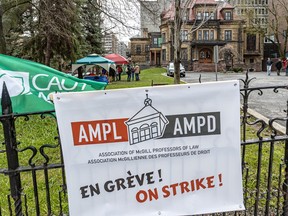 A sign reading Association of McGill Professors of Law On Strike hangs on a fence in front of a university lawn.