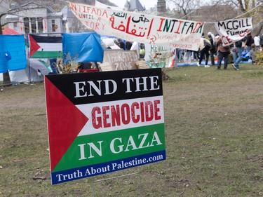 A sign reading 'End the genocide in Gaza' stands on the lawn with an encampment in the background