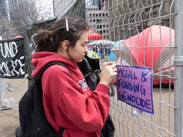 A young woman affixes a sign reading 'McGill is funding genocide' to a fence