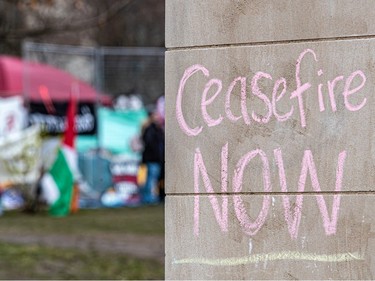 The words 'Ceasefire NOW' are written in chalk on a wall with an encampment visible in the background