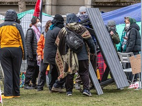 A group of people gather by a picnic bench that has been flipped on its side on the edge of an encampment on McGill's campus